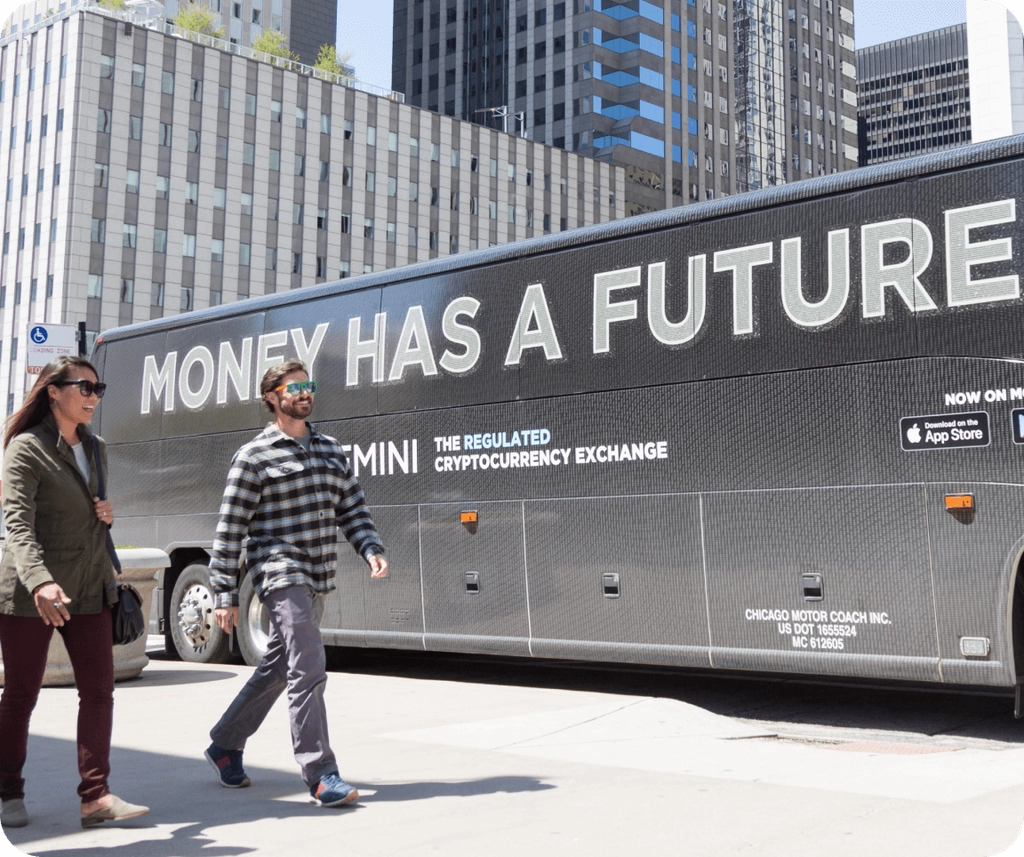Picture of a man and women walking on the sidewalk of NYC next to a bus with a Gemini ad on the side.